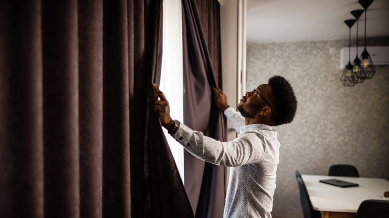 Person opening brown velvet curtains