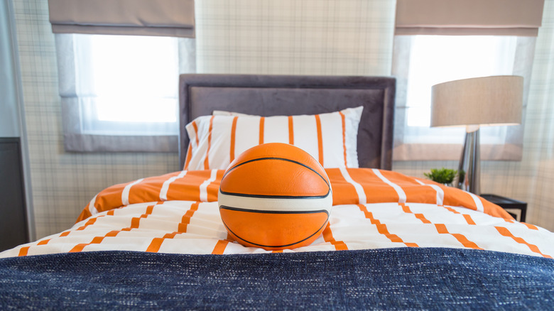 A modern bedroom with orange striped bedding and a basketball on the bed