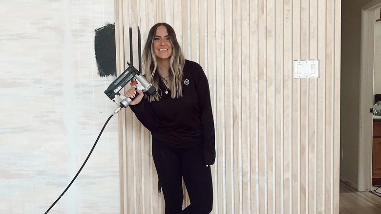 Woman holding nail gun by wall