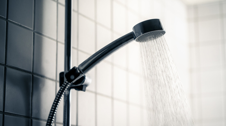 A shower head in a black bathroom has the water turned on