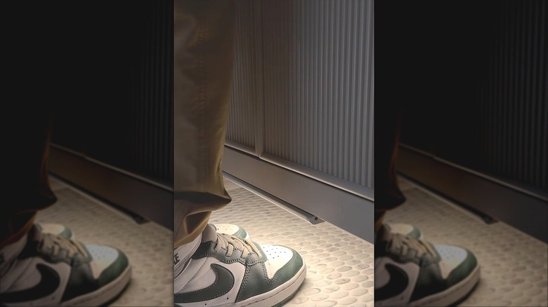 A person's feet in shoes are lit by the under-cabinet light.