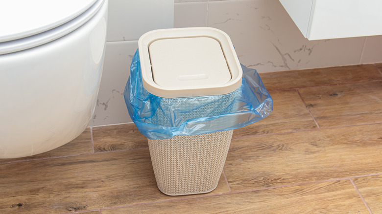 Beige bathroom trash can with lid and blue liner