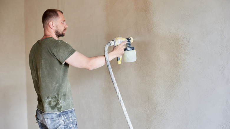 Man using a paint sprayer on a beige wall