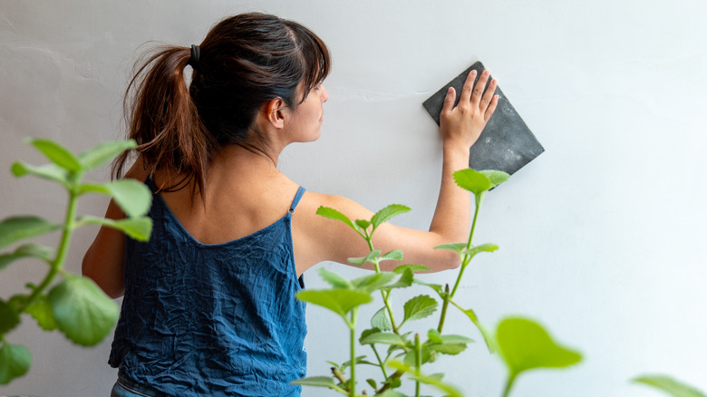 Woman sanding wall with plants in foreground