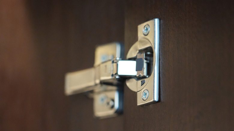 A metal hinge is attached to a wood cabinet