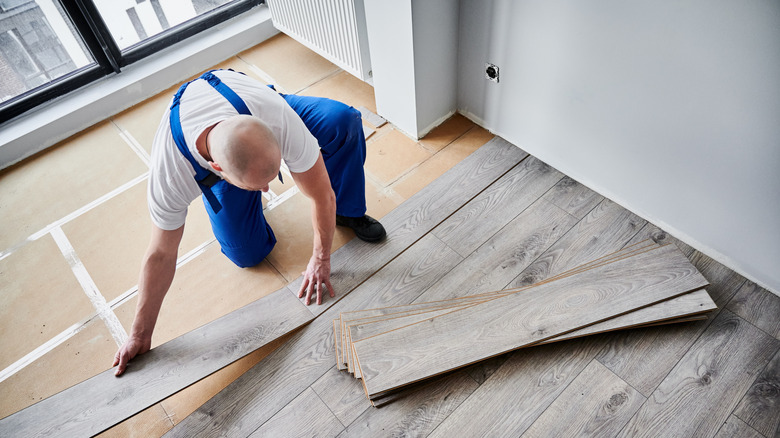 A man in blue overalls lays laminate planks on the floor during installation