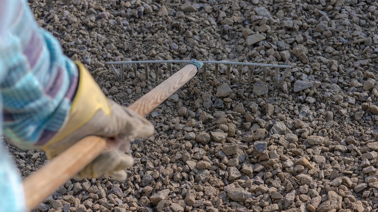 Person with gloves on raking gravel driveway