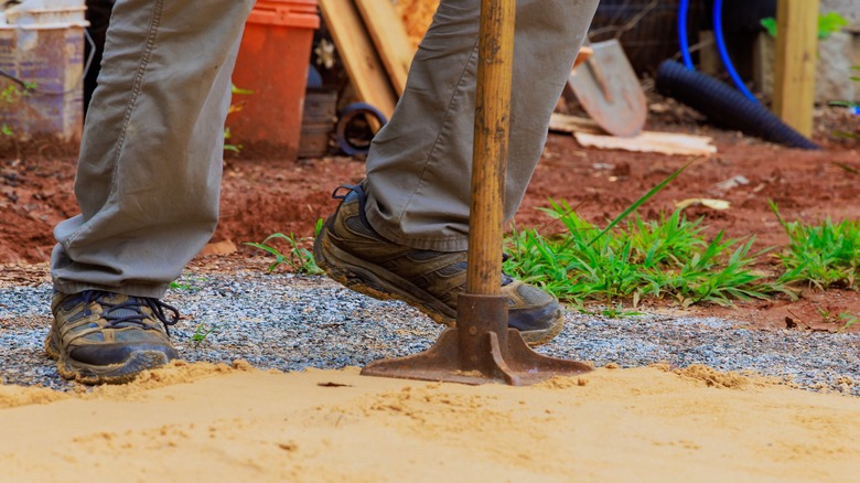 A man using a tamping tool on sand in yard