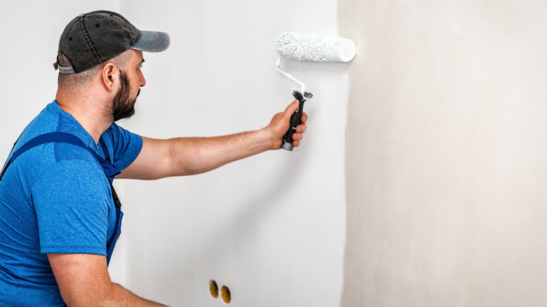 Man painting a beige wall white with a roller