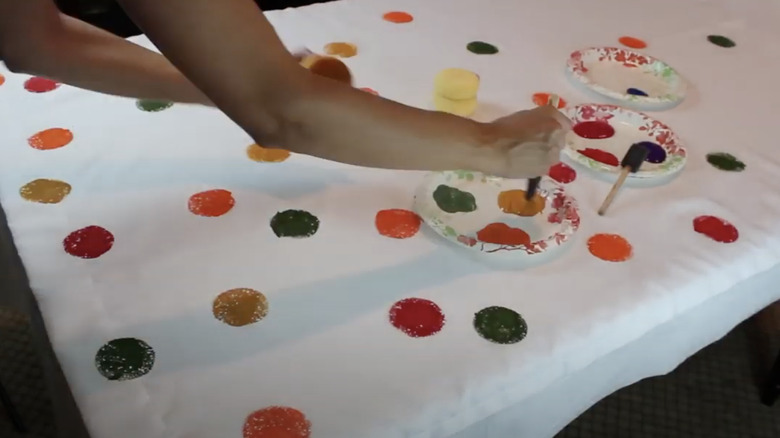 Person paints orange, yellow, red, and green polka dots on a white curtain