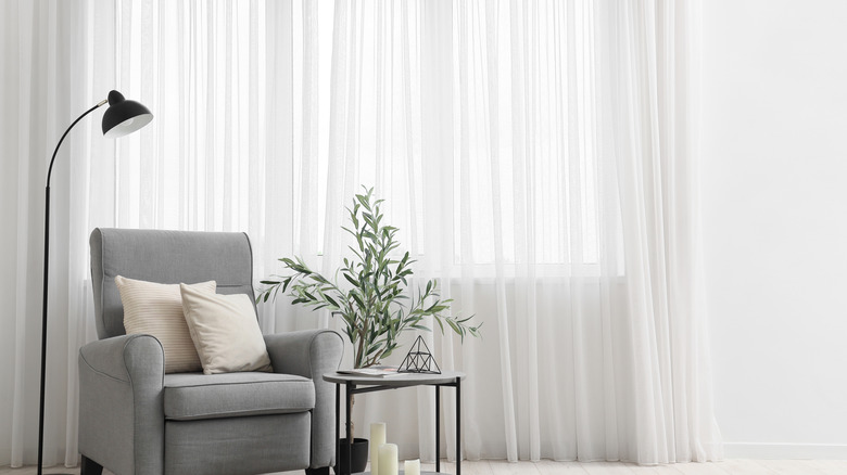 grey armchair and coffee table sit in front of filmy white floor-length curtains