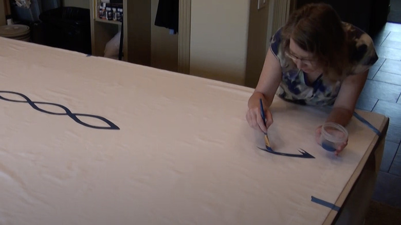 Woman paints a pattern on a white curtain with dark blue paint