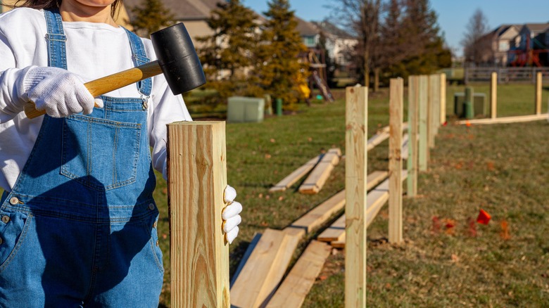 Woman holding hammer to instal fence posts