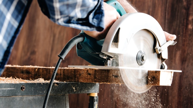 person cutting through end of wood board with circular saw in woodshop