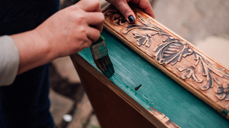 Woman painting wooden drawer with carved design