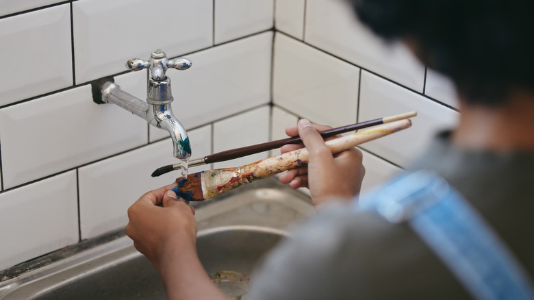 person cleaning paintbrush in sink