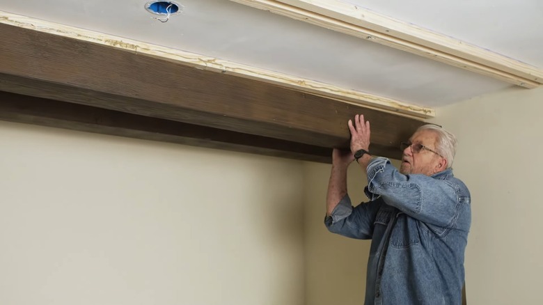 older man installing faux wood beam on ceiling