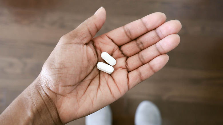 A hand holding two acetaminophen tablets