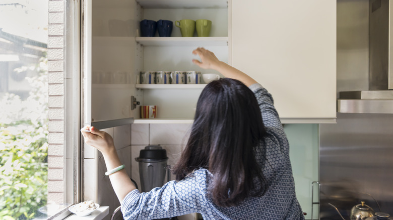 A woman looks through her kitchen cupboards