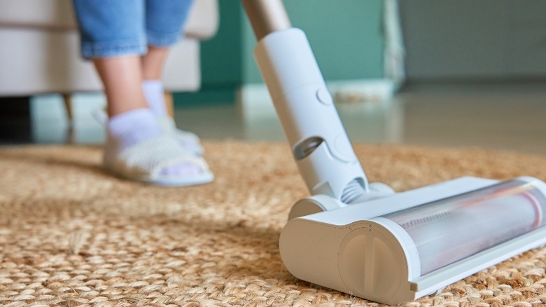 Person in jeans, socks, and sandals vacuuming jute rug