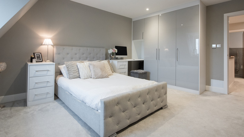 A bedroom with a side table and closet with glossy gray doors.