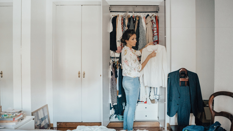 A woman standing in front of her clothes-filled bedroom closet.