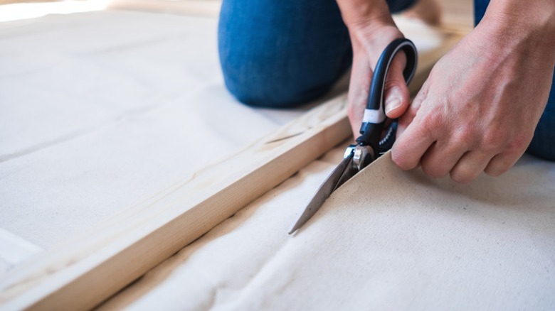 person cutting canvas sheet with wood slat lying on it