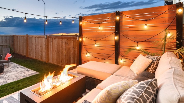 privacy wall with string lights next to patio set with fire pit in fenced-in backyard