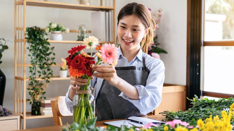 Asian woman florist arranging fresh flowers in a vase