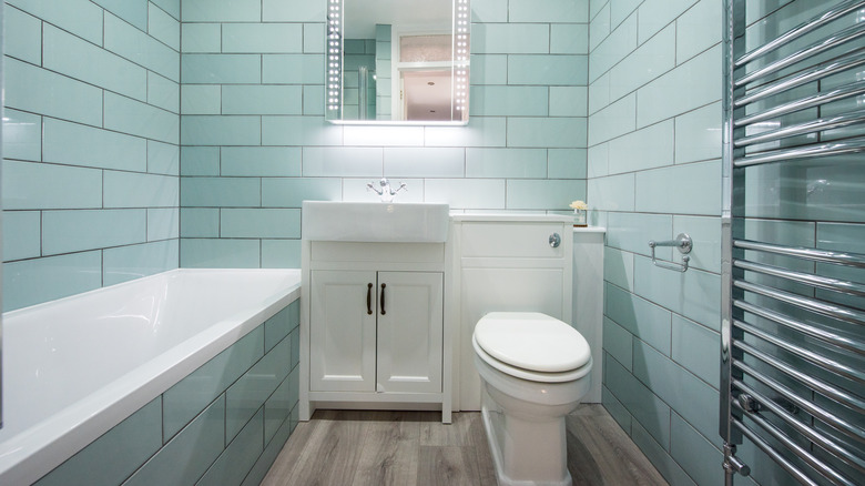 A small, cramped bathroom with a bathtub, sink, toilet, and towel heater.