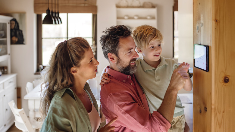 Family looking at smart thermostat, adjusting and lowering heating temperature at home.