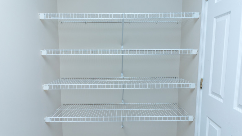 Four long wire closet or pantry shelves rest against a white wall