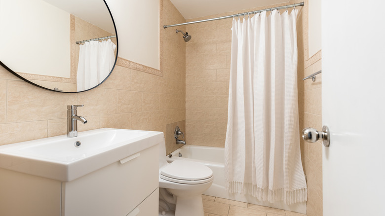 White shower curtain hanging from rod in a small bathroom with white accessories