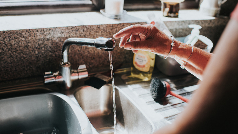 Hand reaches for running kitchen faucet