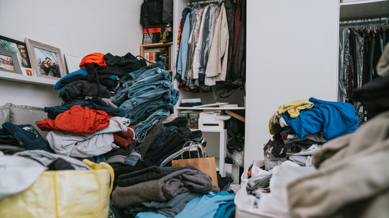 A pile of clothes sits outside of a closet