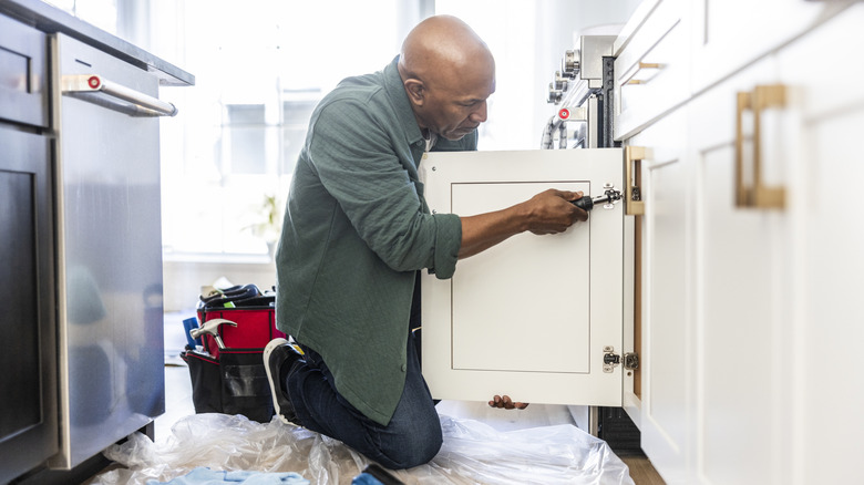 A man working on a cabinet hinge