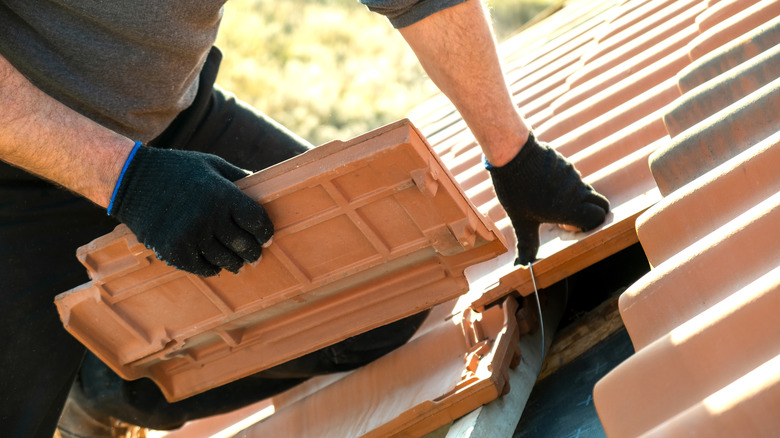 Worker installing red roof tiles