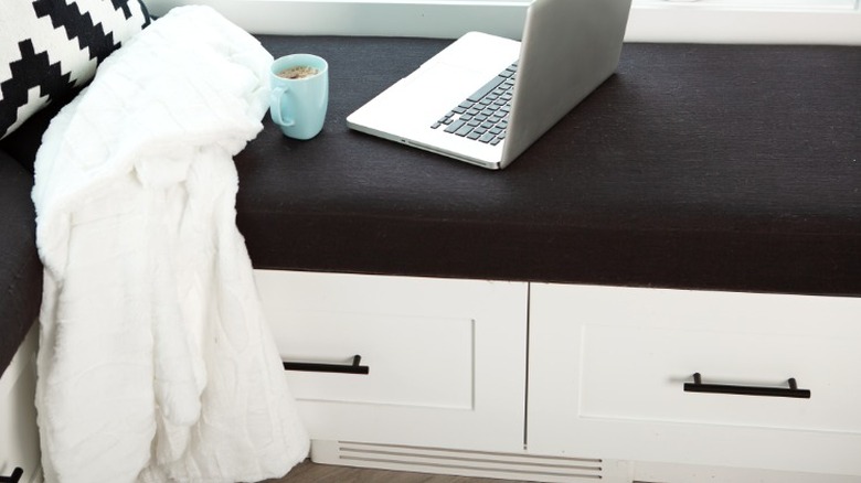 laptop, coffee mug, and white shower robe on modern white breakfast nook with drawers and black upholstered seat