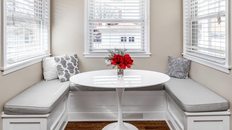 breakfast nook with horseshoe bench and white circular table with red flowers in vase