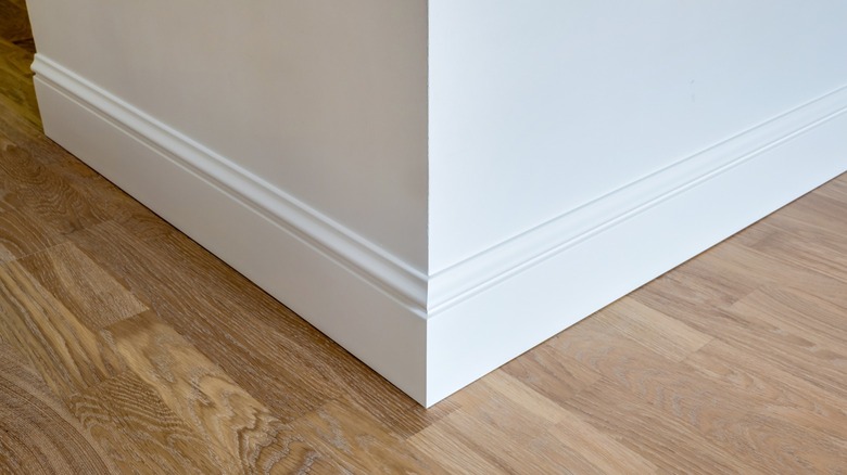 A close-up image of a white baseboard corner with intricate molding and edges.