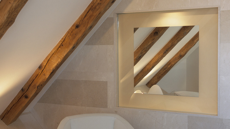 A square mirror with a gold border next to wooden beams