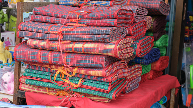 Colorful bamboo beach mats stacked on a chair in a beachside store.