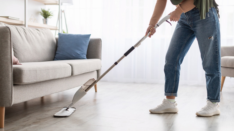 person using Swiffer under couch