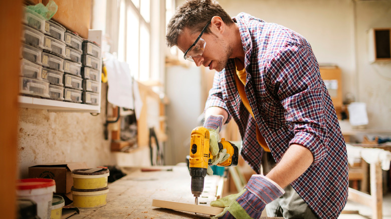 A man in a flannel shirt has drilled all the way through a piece of lumber