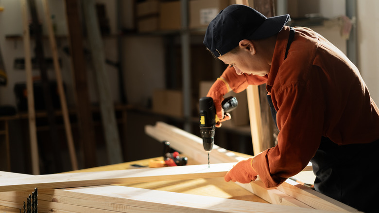 A person in a backward hat drilling into a piece of lumber in a wood shop