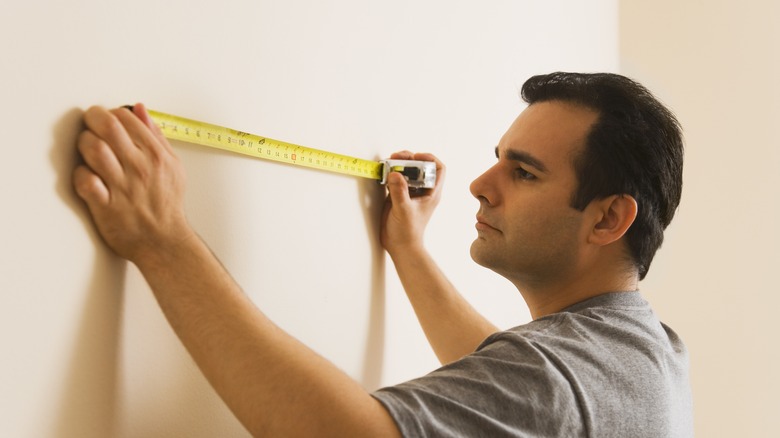 Man using a measuring tape on a wall.