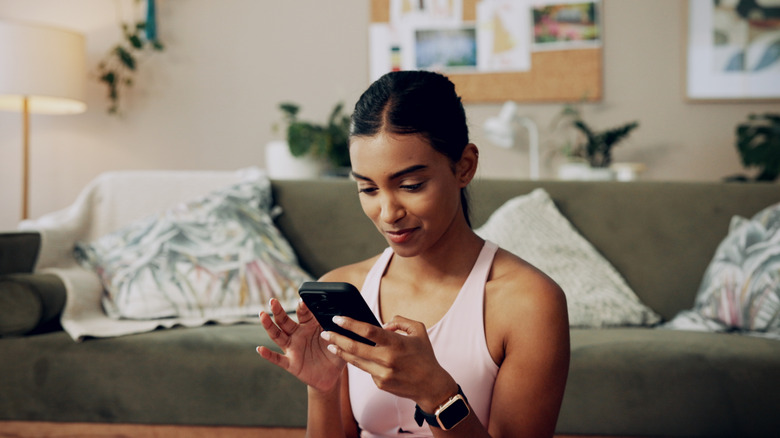 A young woman scrolls through her phone while sitting in a stylish living room