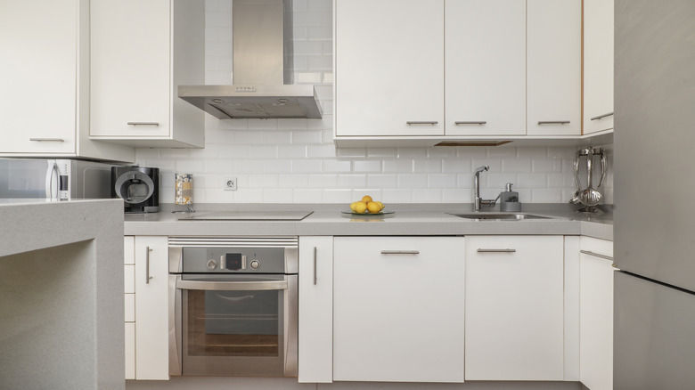 Front image with a kitchen equipped with white furniture, integrated stainless steel appliances, a small island on one side