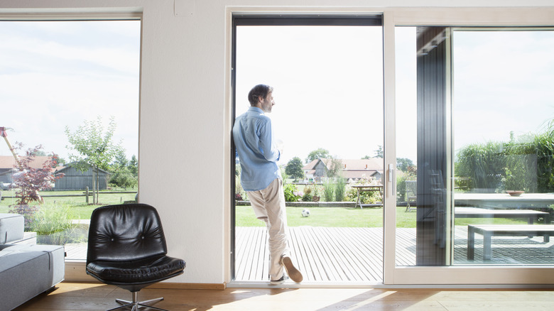 a man stands in doorway of an open sliding glass door leading from house to back deck.