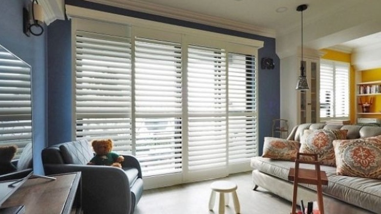 A bright living room with blue walls features bi-fold plantation shutters over a sliding glass door.